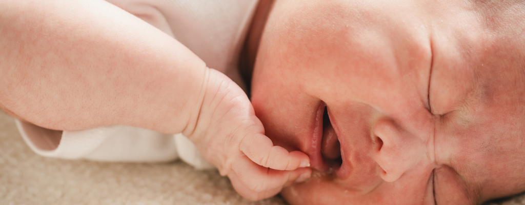 newborn baby expressing discomfort with his hand on lower lip