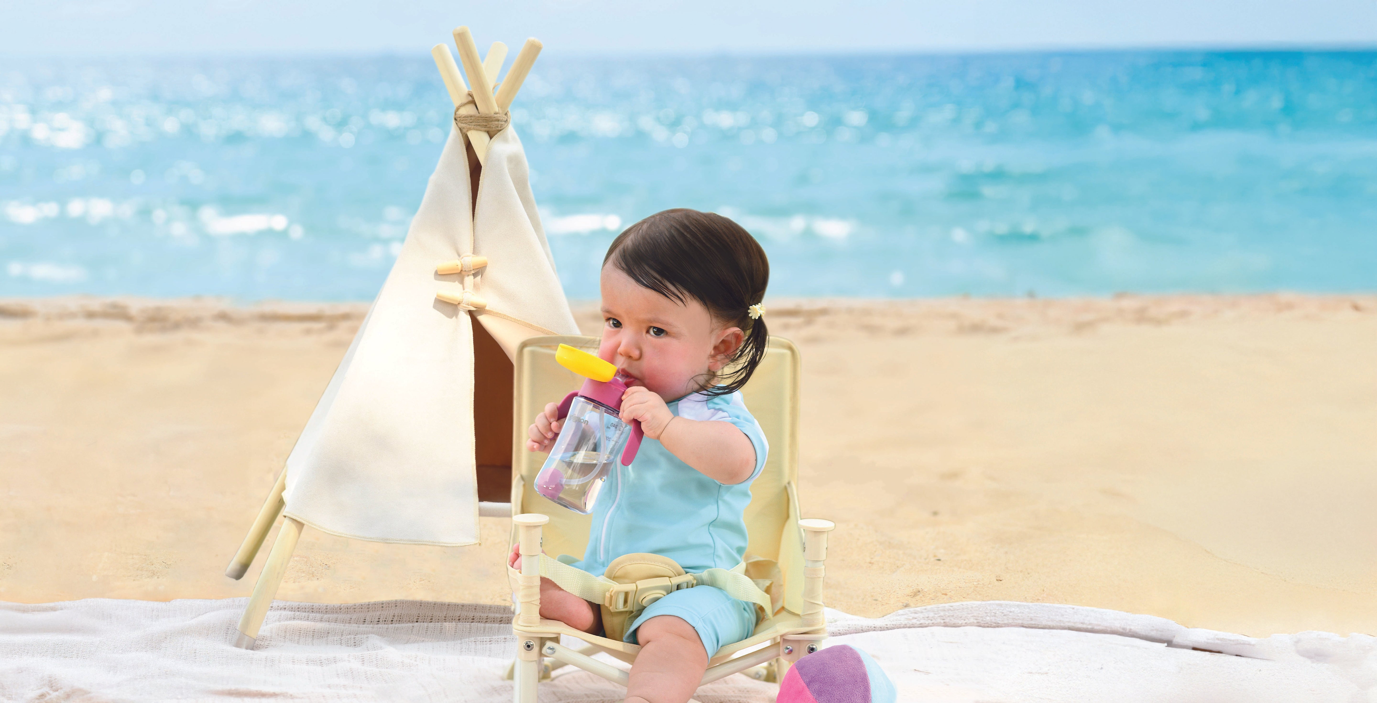 baby drinking from straw cup on beach