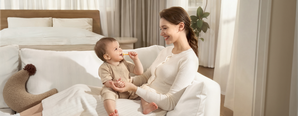 Mother helping her baby brush his teeth and gums with a Pigeon Baby Training Toothbrush while sitting on her lap
