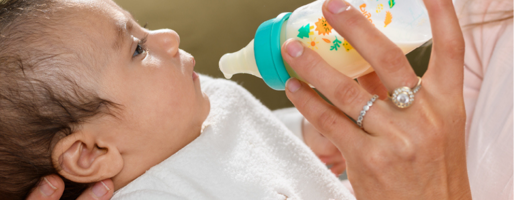 Baby with a Pigeon Flexible Curve anti-colic bottle held in front of his mouth, with milk about to drip from the teat